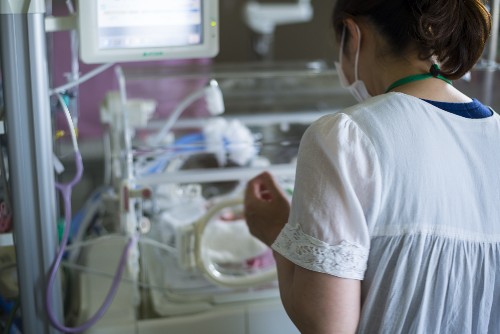 NICU nurse working alongside the incubator of a baby