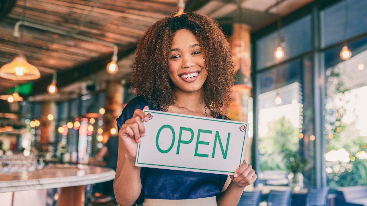 Picture of woman in a store carrying a sign saying "Open"